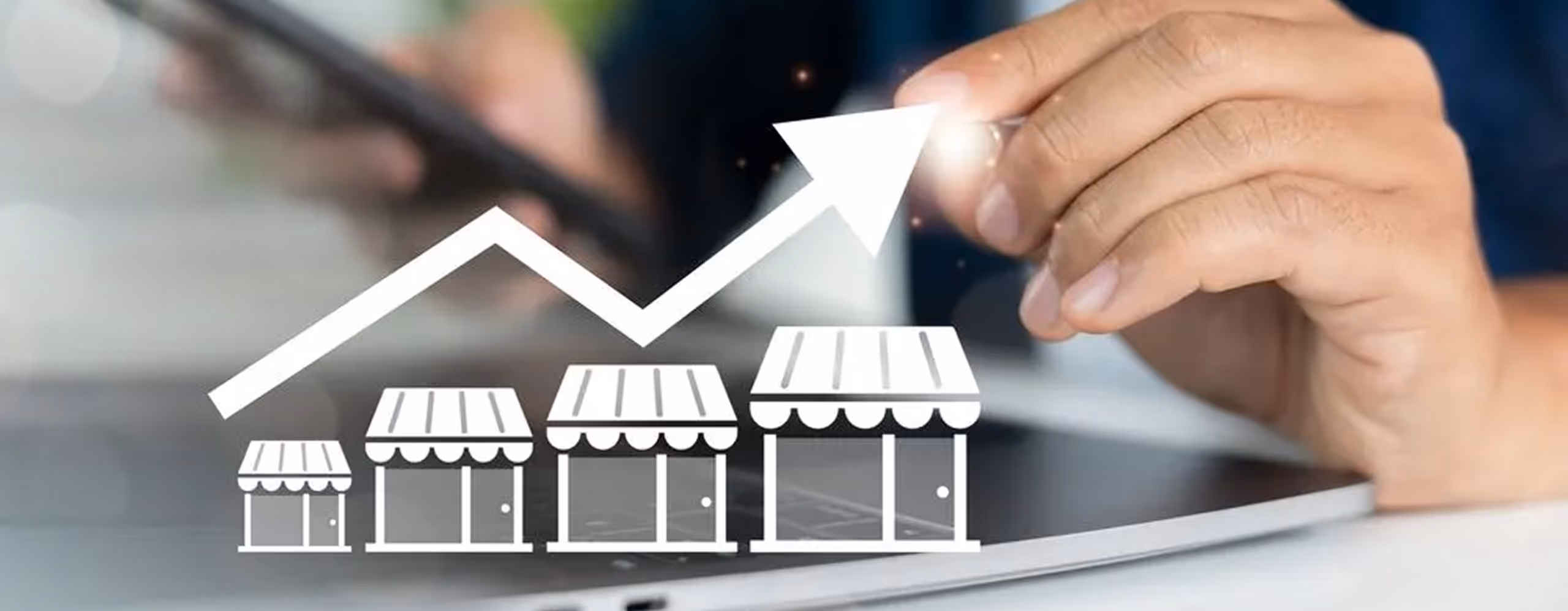 Hand holding a pen pointing at an upward arrow over four increasing store icons on a laptop screen, symbolizing business growth.