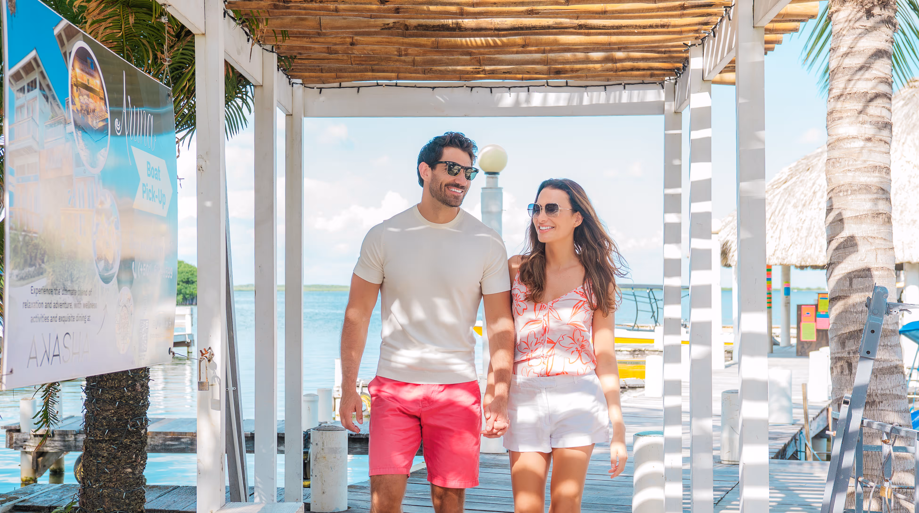 Smiling couple holding hands walking on a wooden dock by the water under a pergola.