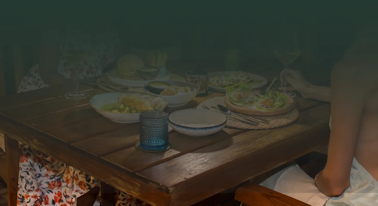 Wooden dining table set with plates of food, glasses of wine, and two people seated, one holding a glass of white wine.