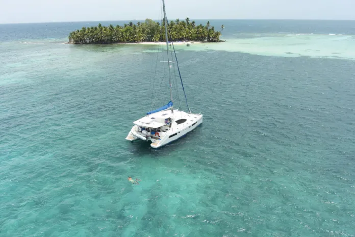 Catamaran anchored in clear turquoise water near a small tropical island.
