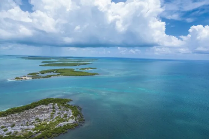 Aerial view of a series of small green islands surrounded by calm blue ocean under a partly cloudy sky.