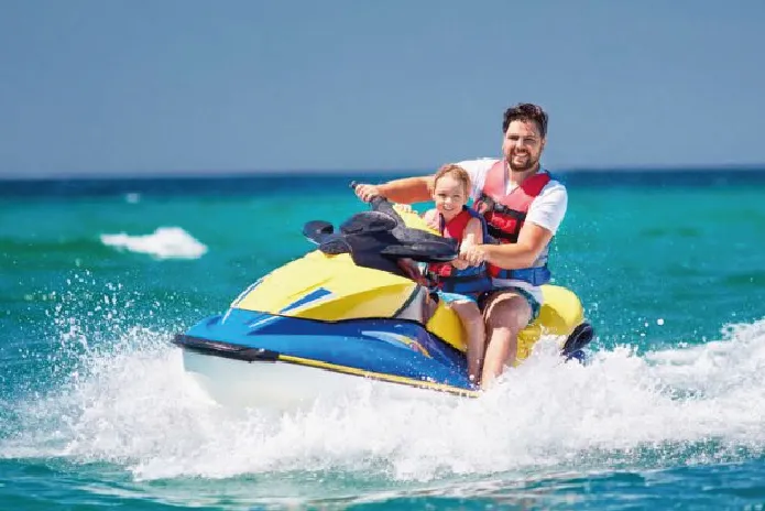 Man riding a jet ski on the ocean, smiling while speeding over waves.