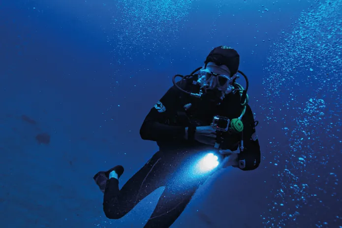 Scuba diver underwater shining a flashlight while giving an OK hand signal.