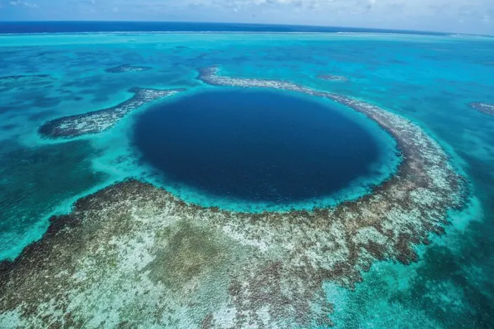 Aerial view of a large, circular blue hole surrounded by coral reefs and turquoise waters in the ocean.