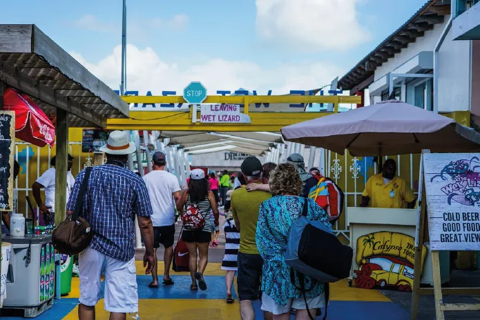 Crowded outdoor market with people walking between vendor stalls under umbrellas.