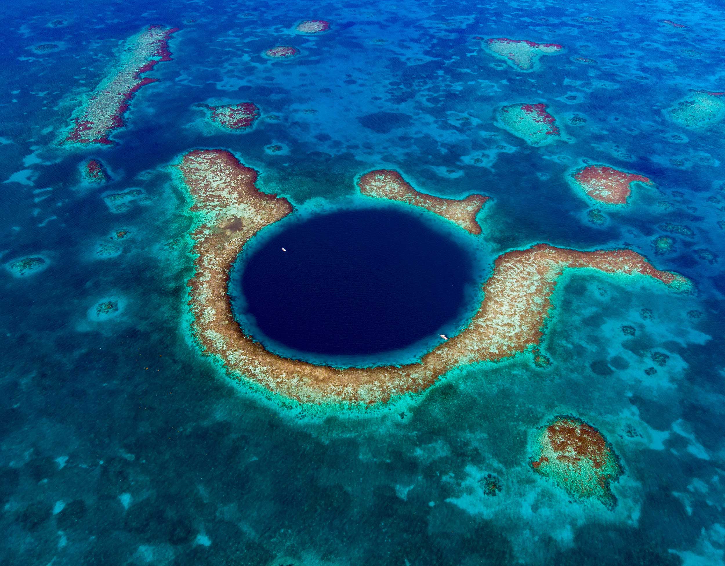 Aerial view of the Great Blue Hole, a large underwater sinkhole surrounded by coral reef in clear blue ocean waters.