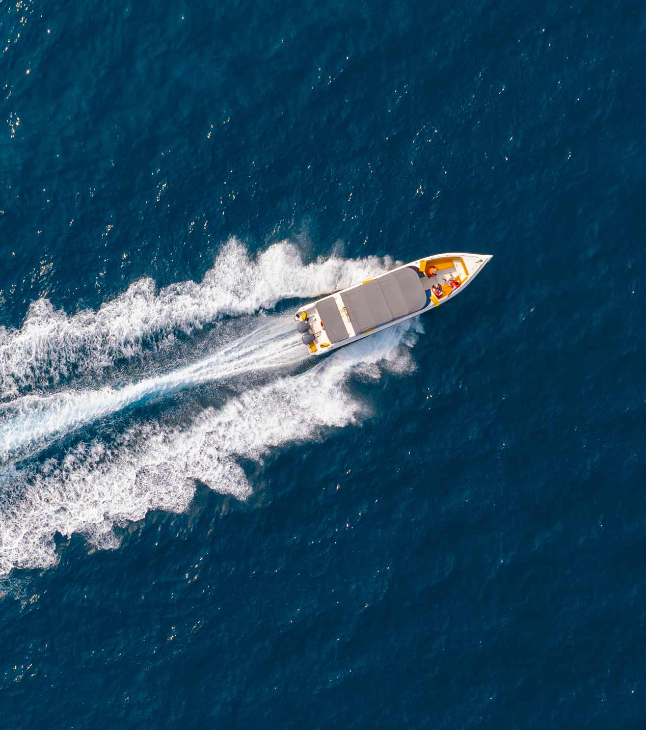 A fast motorboat with passengers creating a white wake as it moves across deep blue water.
