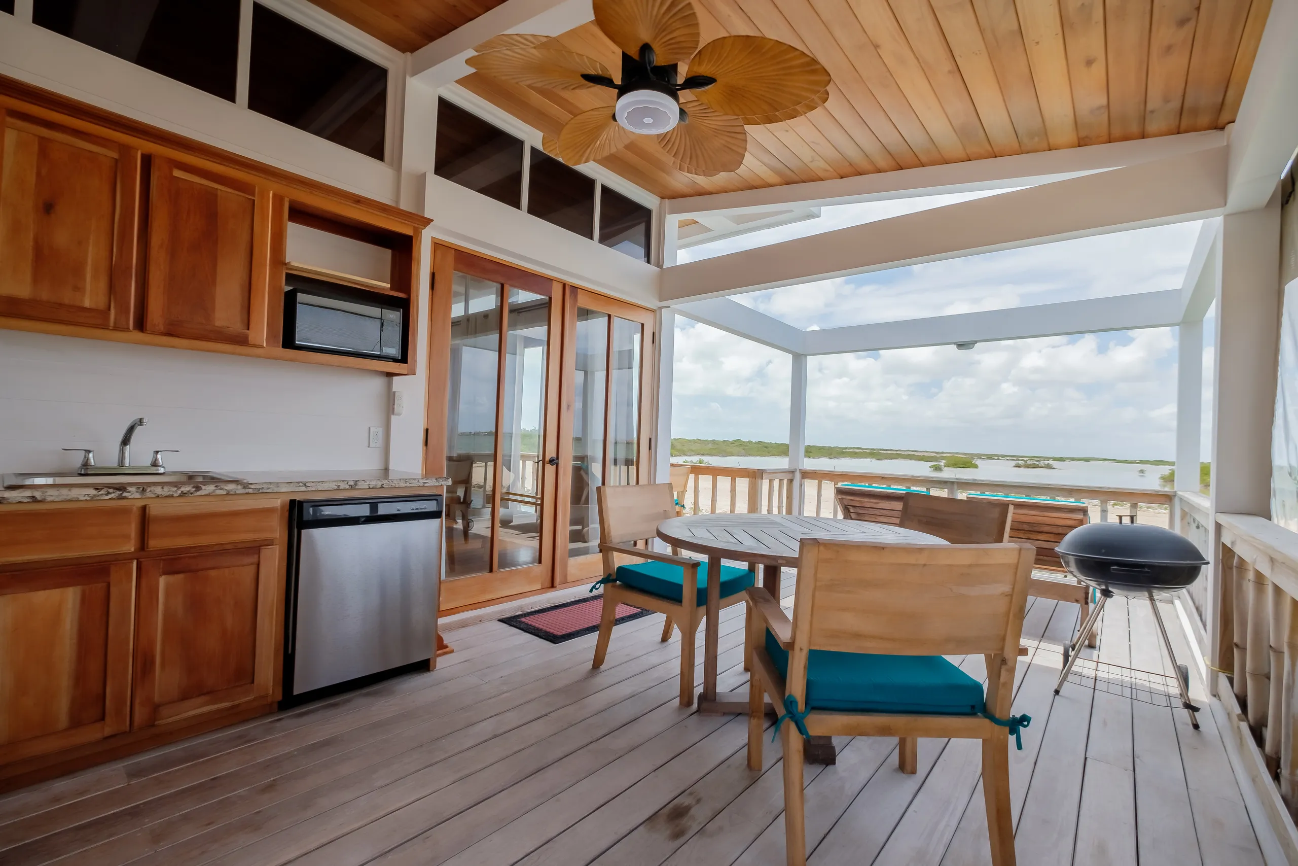 Outdoor patio kitchen with table, chairs, grill, and water view.