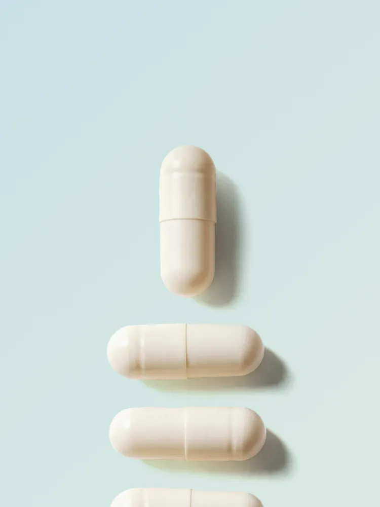Four white capsules arranged vertically on a pale blue background, each casting a soft shadow to the right.