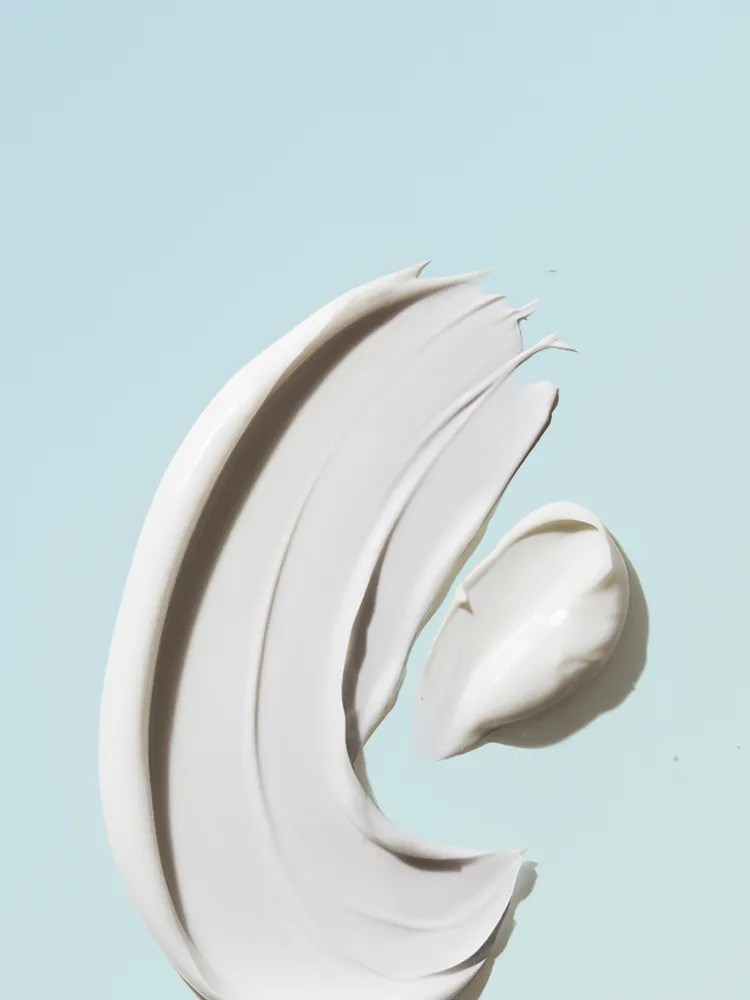Smears of white cream on a light blue background, showing smooth texture and glossy finish.