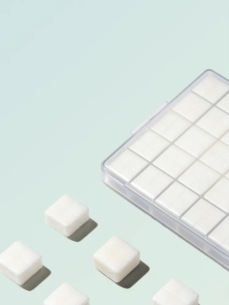 A clear plastic container filled with white, square-shaped troche tablets on a light blue surface, with several troches scattered nearby.
