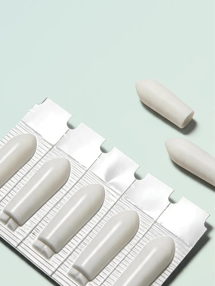 Close-up of white suppositories in silver blister packaging with two suppositories removed and placed beside it on a light surface.