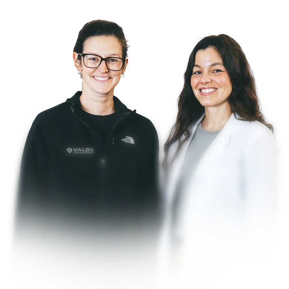 Two smiling women standing side by side, one wearing glasses and a black zip-up jacket with a Valor logo, the other in a light-colored blazer and grey top.