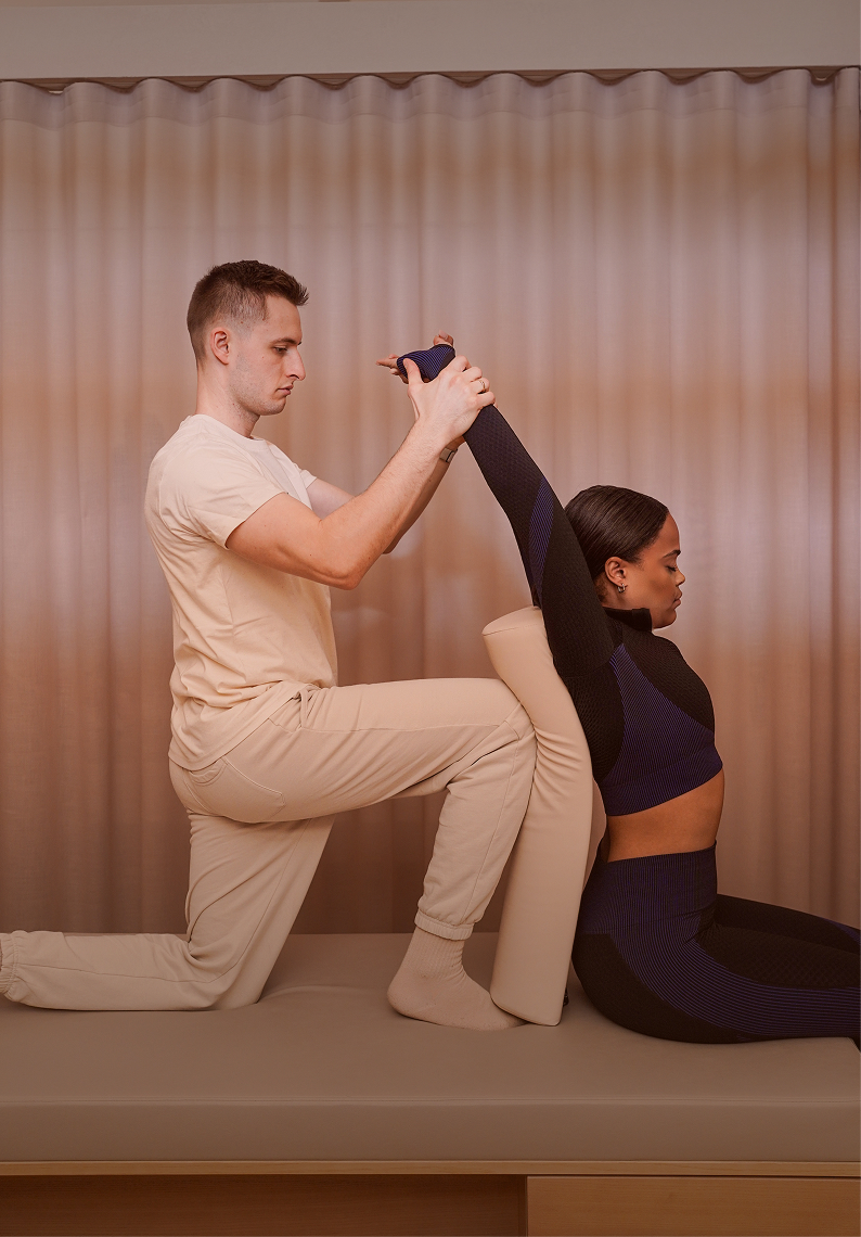 Assisted Stretch: Expert dehnt das Bein einer knienden Kundin