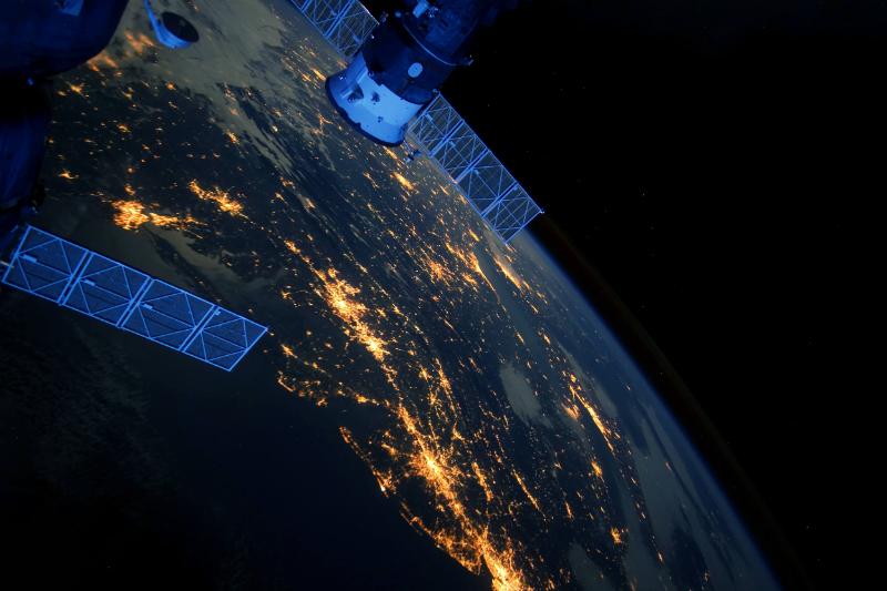 Young man in a dark hoodie thoughtfully looking at a computer screen in a dimly lit room.
