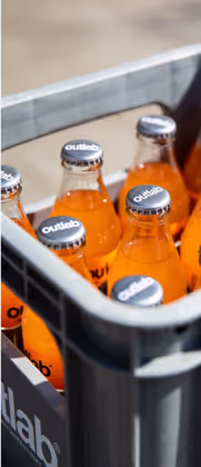 Garrafas de refrigerante laranja Outlab em um recipiente plástico cinza.