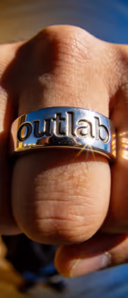 Mão fechada com anel metálico prateado gravado com a palavra 'butlab'.