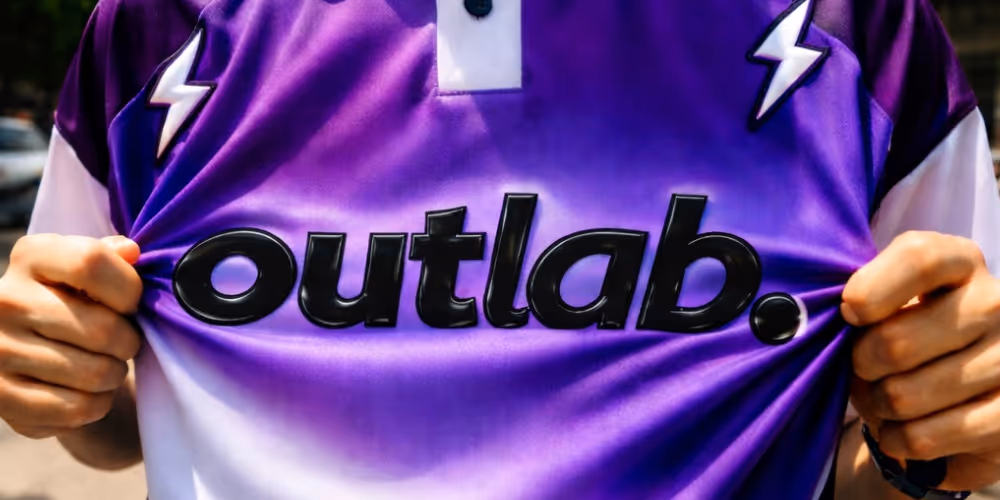 Pessoa segurando uma camiseta roxa com a palavra preta 'outlab.' escrita na frente.