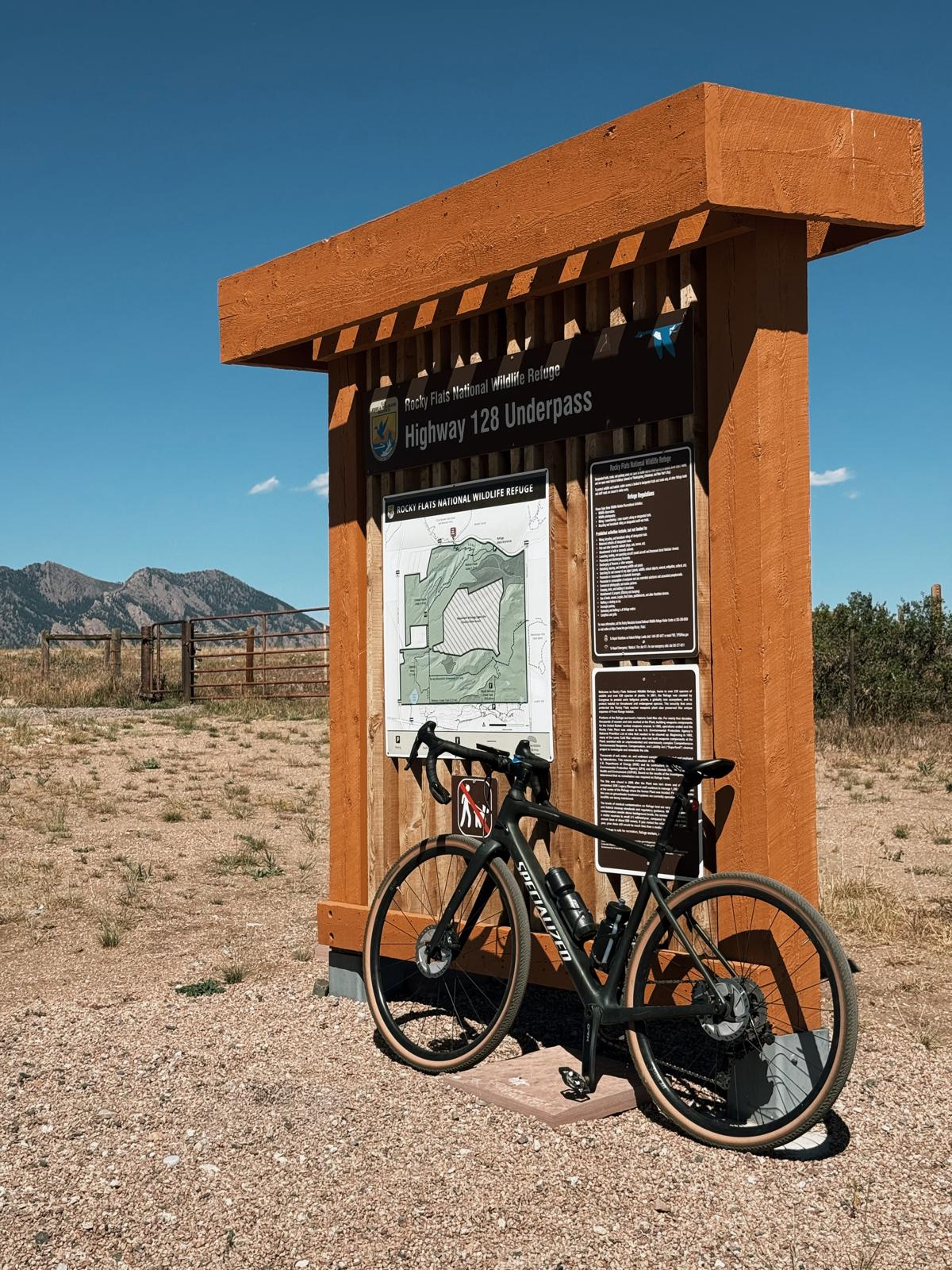 A bicycle parked beside the Rocky Flats National Wildlife Refuge trailhead sign and Dylan’s visitor map.
