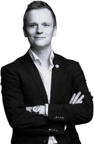 Mustapukuinen mies, valkoinen paita, kädet ristissä, mustavalkoinen kuva.