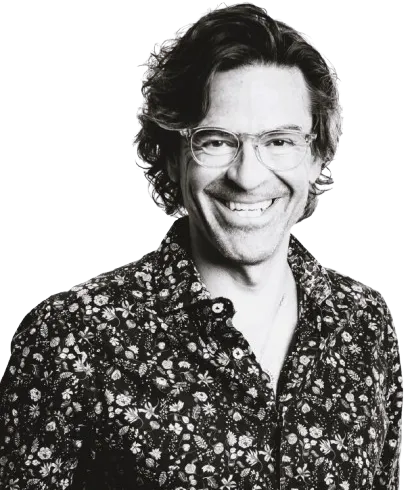Mustavalkoinen kuva hymyilevästä miehestä, jolla on silmälasit ja kukkakuvioinen paita.