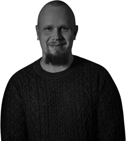 Mustapartainen mies tummassa neuleessa, valaistus on pehmeä ja kuva on mustavalkoinen.