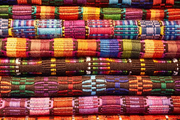 Stack of colorful woven fabric with geometric patterns in various vibrant shades.
