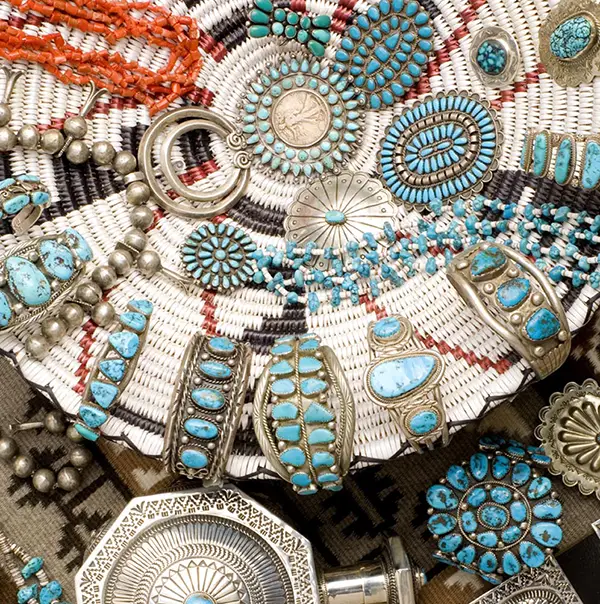 Collection of silver jewelry featuring turquoise stones displayed on woven and patterned fabric.