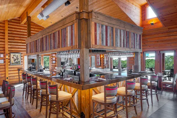 Green courtyard with a stone pathway leading to a circular flowerbed fountain and a brown and white horse standing on the grass.