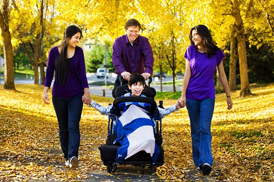 Une famille se promène dans un parc en automne, l'enfant se déplaçant en fauteuil roulant