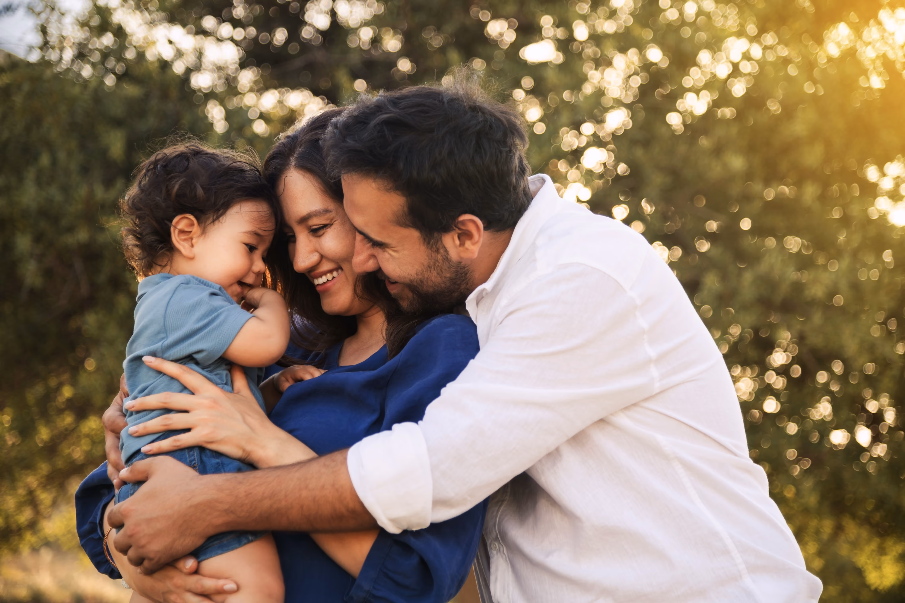 A smiling couple embracing their young child outdoors at golden hour
