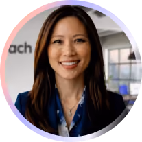Smiling woman with long dark hair in a blue blazer in a modern office setting.