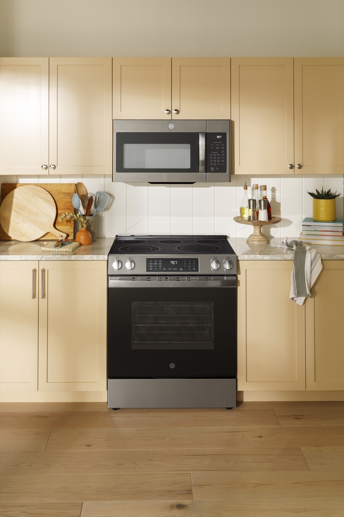 GE stainless steel range and microwave in a sunlit kitchen with warm wood cabinetry