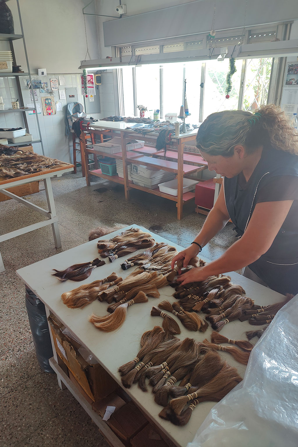 Woman organizing bundles of hair on a white table in a well-lit room.