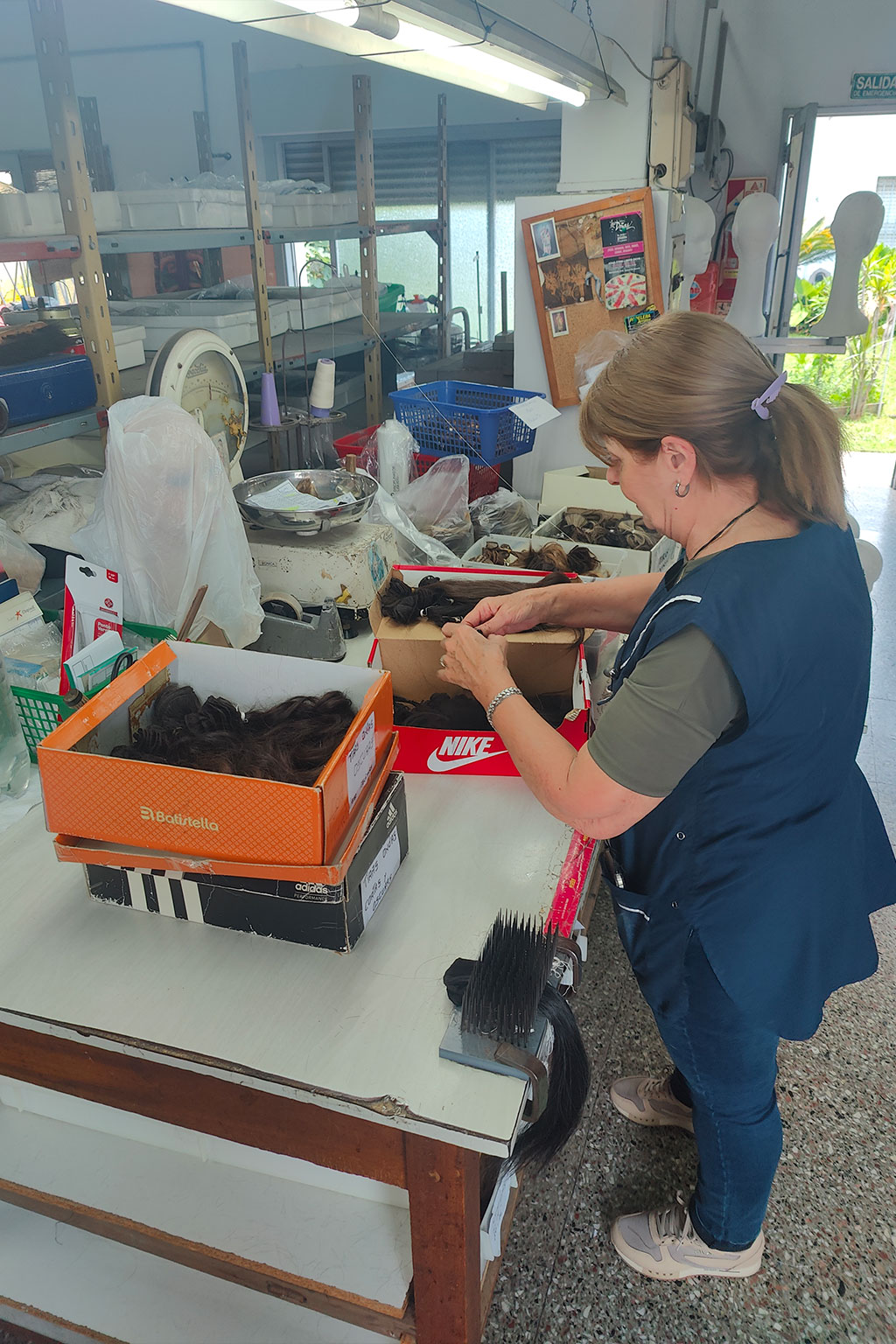 Woman organizing bundles of hair in boxes on a workbench inside a workshop.