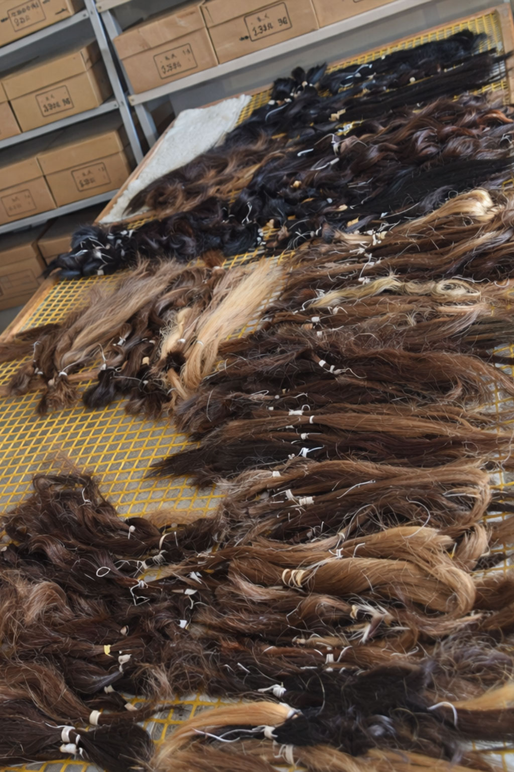 Bundles of varied shades of brown and black hair extensions spread out on a yellow mesh table in a storage room.