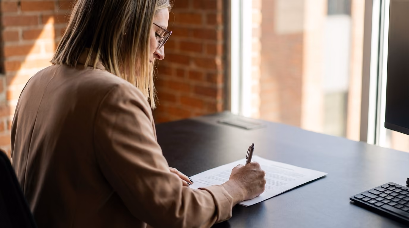 Ashley Kunkle, CEO, writing on a document at her desk by a window