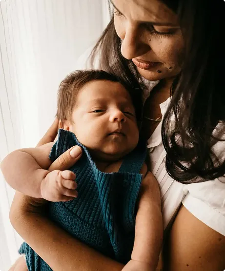 Mother gently holding and looking at her newborn baby wrapped in a knitted blue outfit.