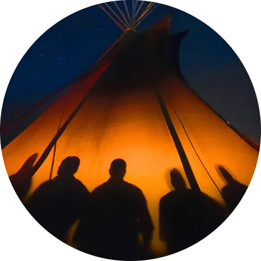 Silhouettes of four people in front of a glowing, illuminated tipi at night under a starry sky.