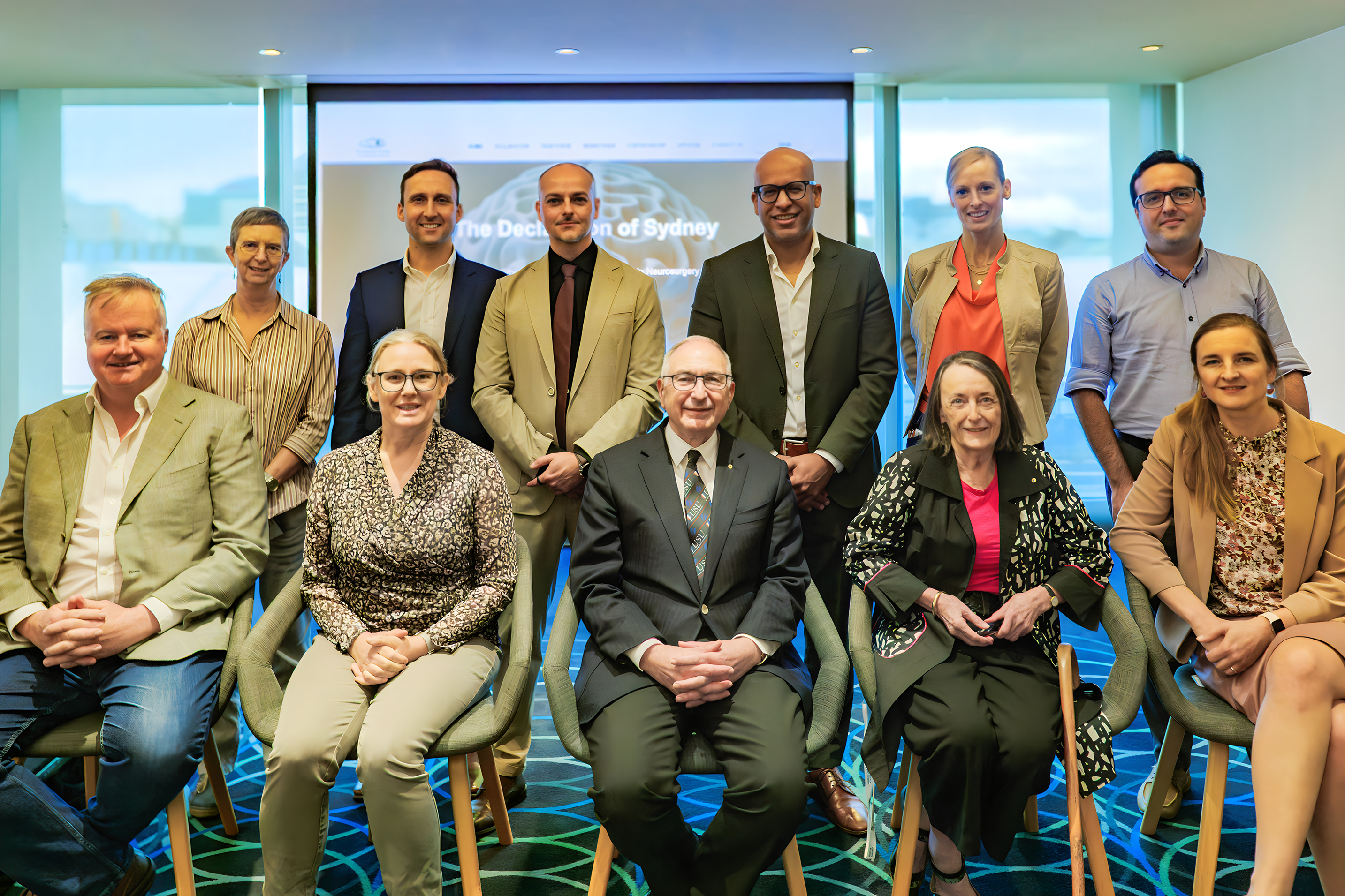 Group portrait of eleven professionals, six standing and five seated, in a modern conference room with a presentation screen behind them.