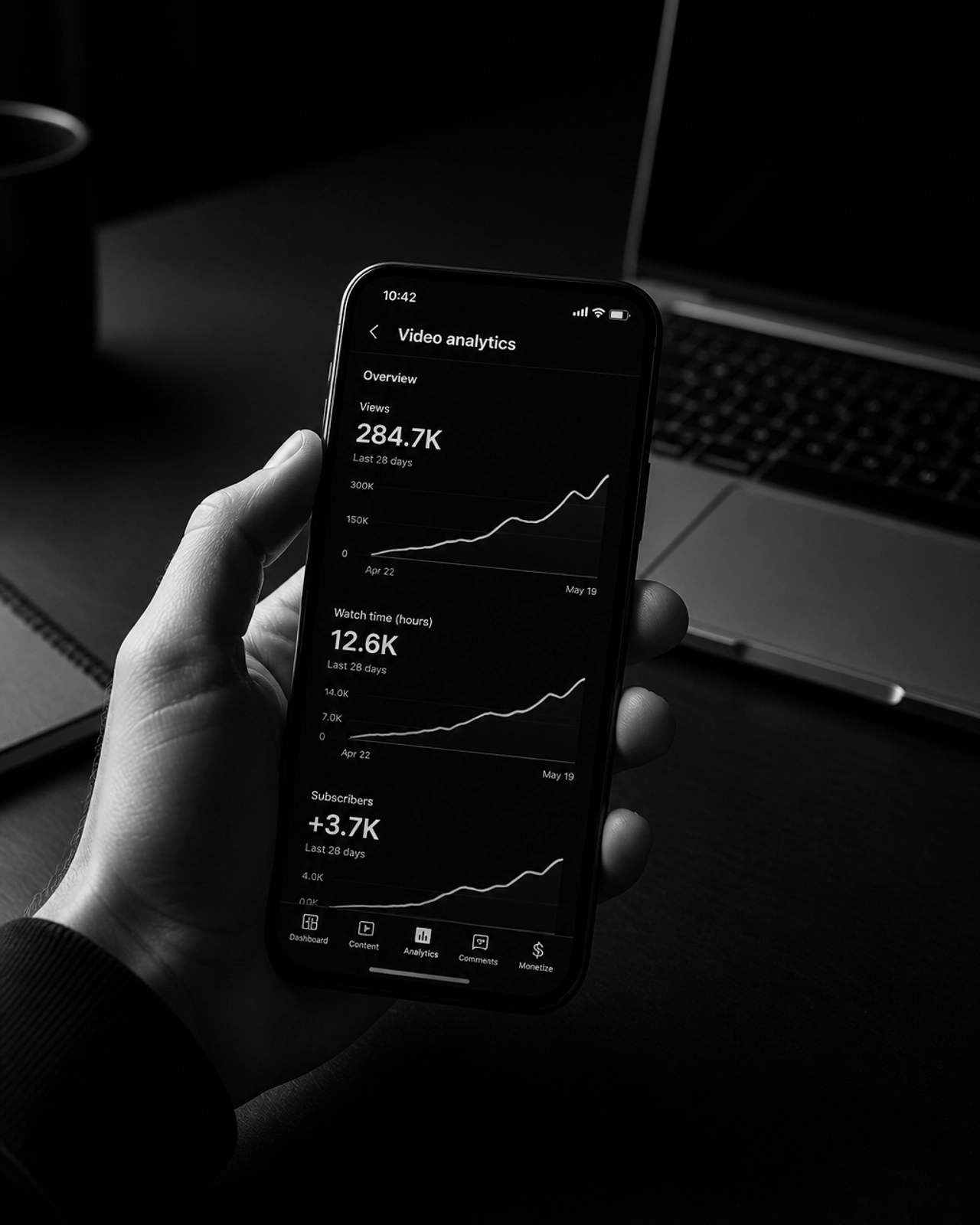 B&W shot of a hand holding a smartphone showing rising analytics graphs