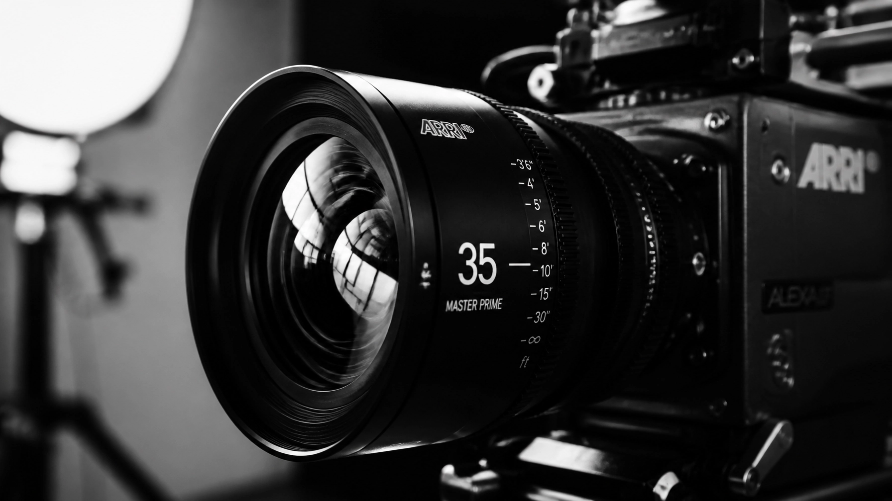 A close-up, high-contrast black and white photo of a high-end cinema camera lens reflecting a studio light. Modern and sleek.