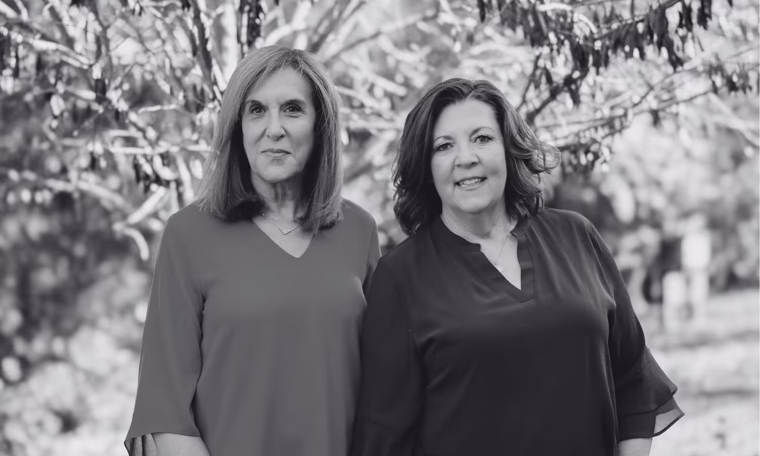 Black and white photo of Mary Harkins and Geri Perkal of Gemsight,  standing outdoors with trees in the background, both smiling gently. Gemsight College Consulting and Career planners are CEP Board-Certified Educational Planners and Expert College Admissions Consultants with over 40 years of combined experience. 