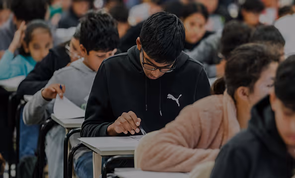 Students seated in rows focused on writing during a test or exam in a classroom.