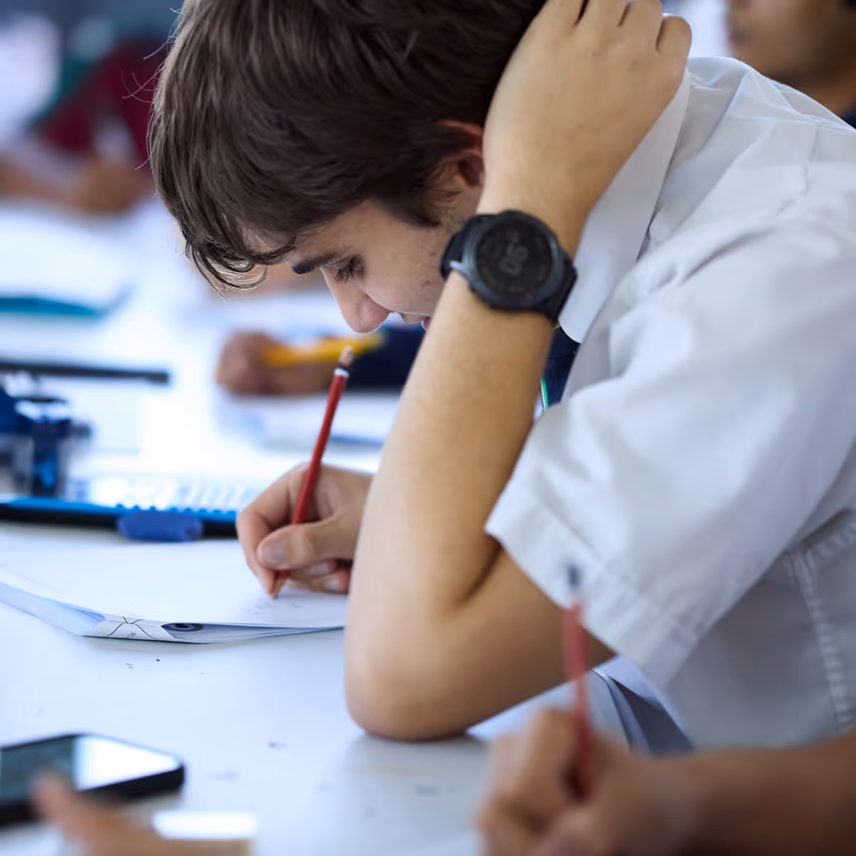 Student in a white shirt concentrating on writing with a pencil during a test or study session.