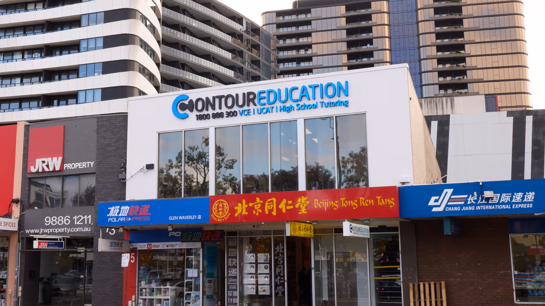 Street view of commercial buildings featuring Contour Education, Beijing Tong Ren Tang pharmacy, Polar Express, JRW Property, and Chang Jiang International Express signage.