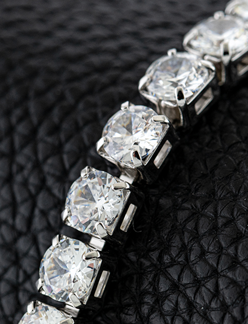 Close-up of a silver bracelet with large, round-cut clear gemstones on textured black leather.