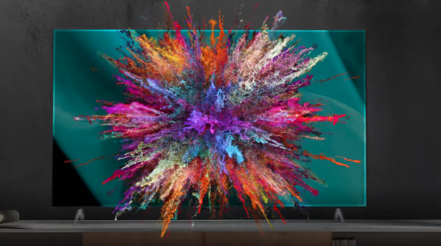 Modern flat-screen TV on a stand showing a vibrant explosion of multicolored powder against a teal background.