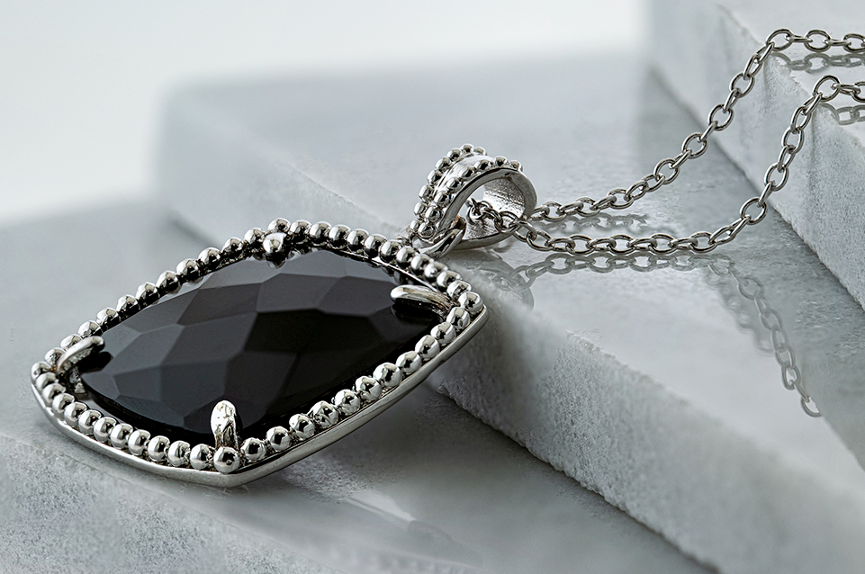 Silver pendant necklace with a faceted black gemstone resting on gray stone steps.