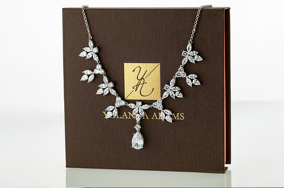 Elegant silver necklace with teardrop and leaf-shaped clear gemstones displayed on a brown Yolanda Adams branded box.